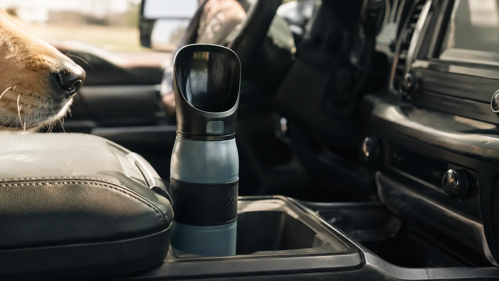 A dog in the back seat of a pickup truck looking at a travel water bottle on the center console